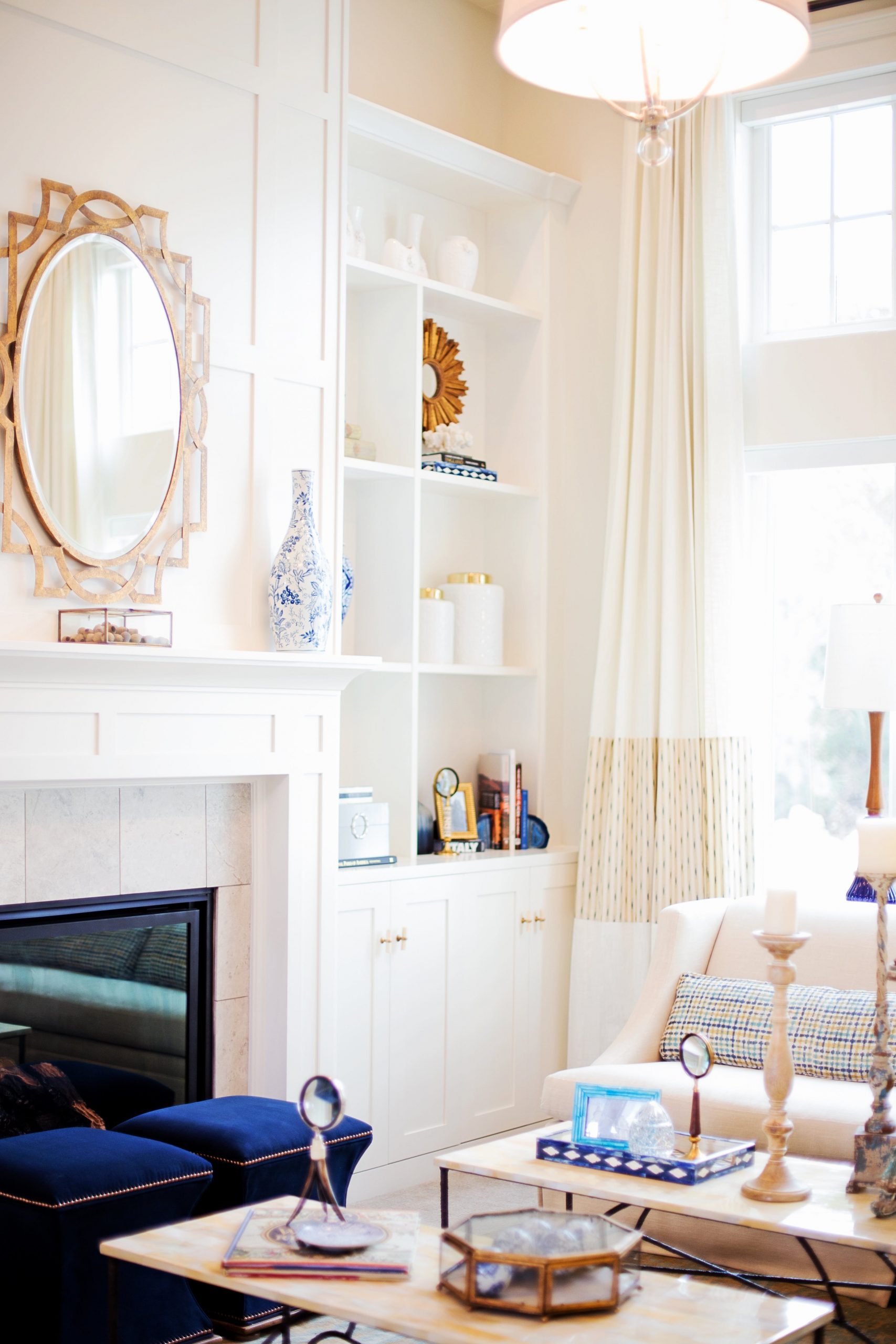 Corner of a bright and welcoming living room, showing a cozy fireplace, built in shelving, and tall windows