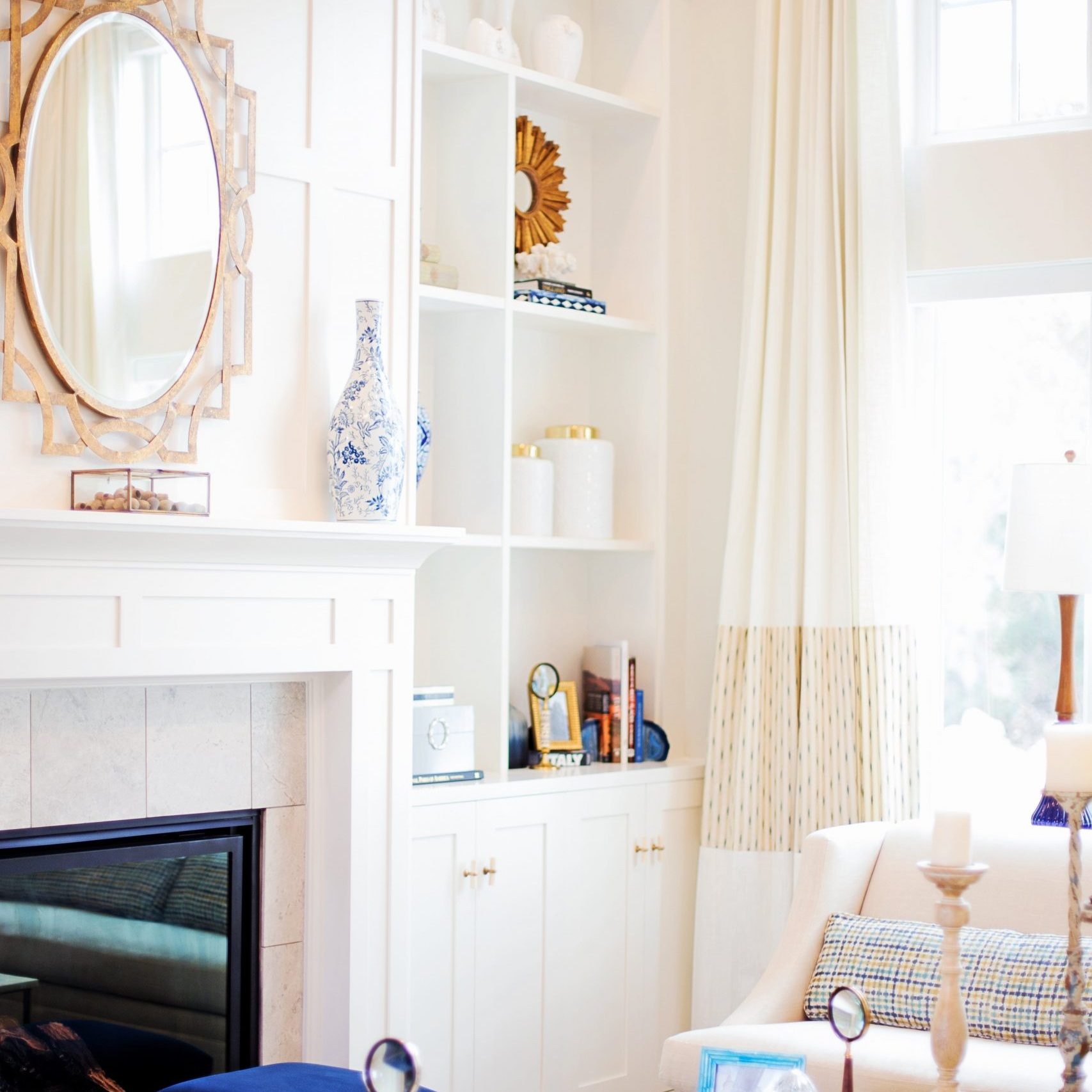 Corner of a bright and welcoming living room, showing a cozy fireplace, built in shelving, and tall windows